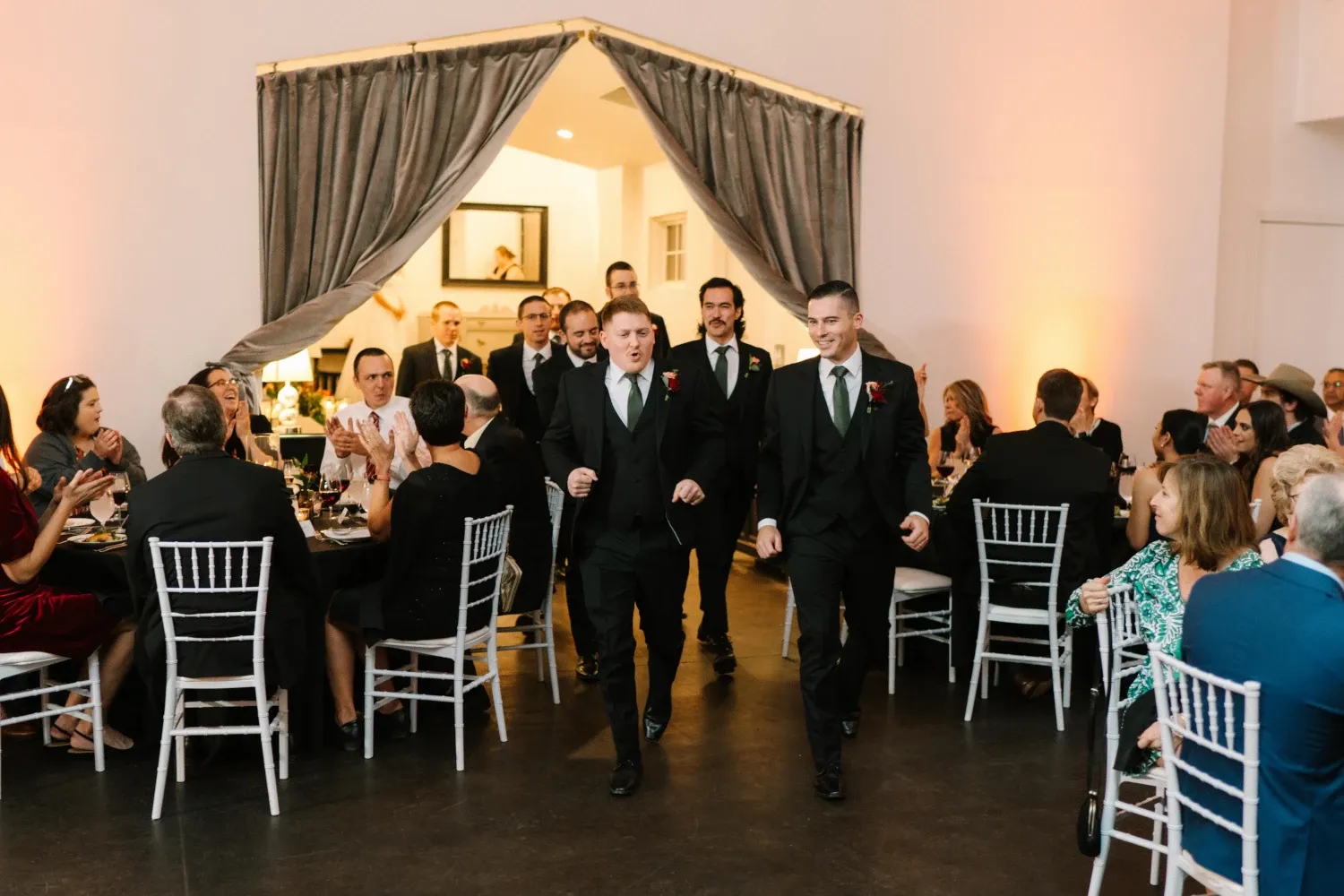 Groomsmen entering wedding reception while guests cheer during DJ announced grand entrance